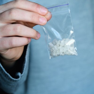 A man in a blue shirt holding a plastic bag containing white crystals. 